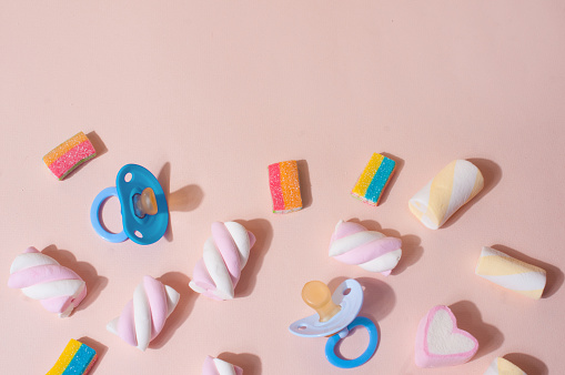 Colorful cute top view flat lay light pink background with baby concept objects with pacifier, candies and marshmallow negative space