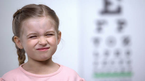 bambina accigliata, cercando di vedere la lettera sul tavolo di prova della vista visione offuscata - strizzare gli occhi foto e immagini stock