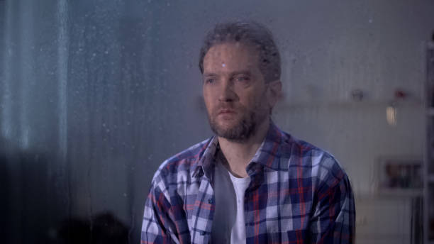istock Lonely sad middle-aged man looking through rainy window, bad weather conditions 1169983360