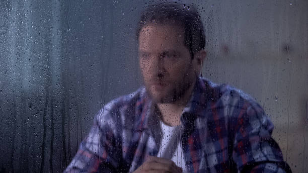 istock Depressed man looking through rainy window, poverty and unemployment concept 1169983415