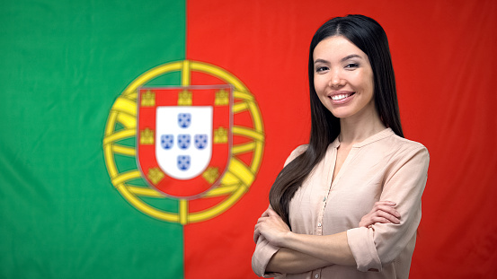 Smiling woman standing with hands crossed against Portuguese flag background