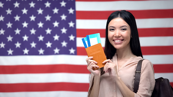 Excited woman holding passport and flight tickets against USA flag background