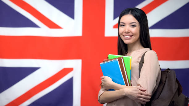 istock Cheerful Asian woman standing against British flag background, study abroad 1169984311