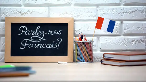 Photo of Do you speak French written on board, France flag standing in box, language