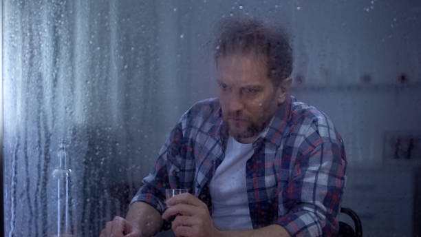istock Alcohol addicted man looking at vodka bottle in loneliness behind rainy window 1169984618