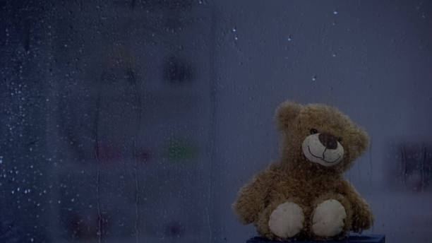 istock Teddy bear on sill behind rainy window, bad weather, hope and support concept 1169984786