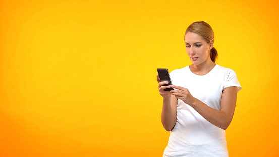 Attractive young woman in white t-shirt using phone app on bright background