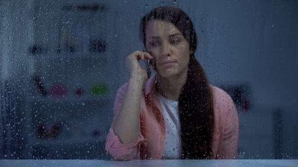 istock Upset middle-aged lady talking phone behind rainy window, bad news, conversation 1169985468