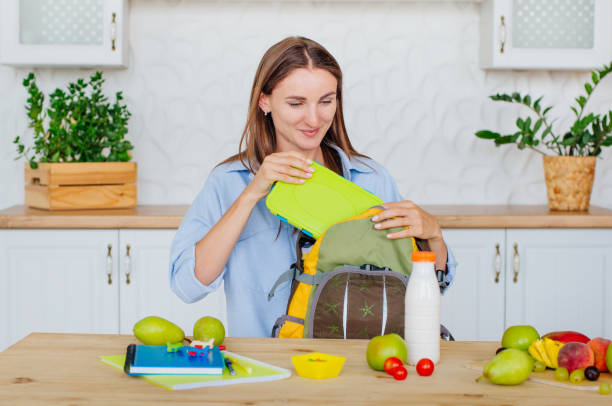 Mother packing lunch box into a kid's backpack Healthy food concept. Mother packing lunch box into a kid's backpack in the kitchen. bag lunch stock pictures, royalty-free photos & images