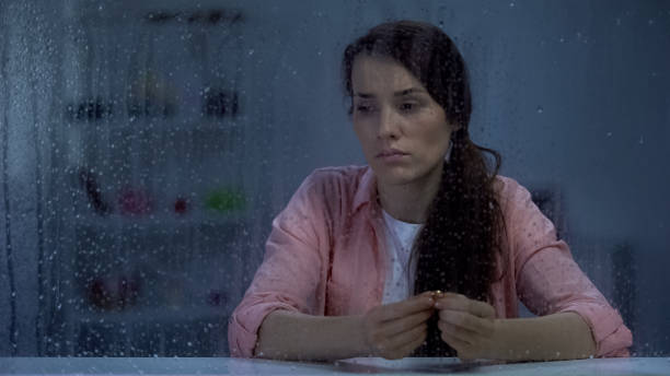 istock Disappointed female holding engagement ring behind rainy window, break up 1169985534