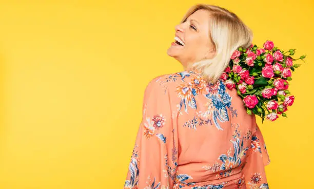 Photo of Holiday event. Mother's day. St. Valentines day. Birthday. Portrait of happy cute lovely senior woman in party colorful clothes with large bouquet of flowers on yellow background