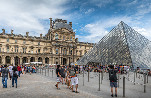 Paris, France - August 4, 2019: The central entrance courtyard to the Louvre Museum surrounded in summer by an overwhelming crowd of tourists in Paris, France. Opened at the end of the 18th century, the Louvre Museum is the most important museum in France and one of the most visited in the world.
