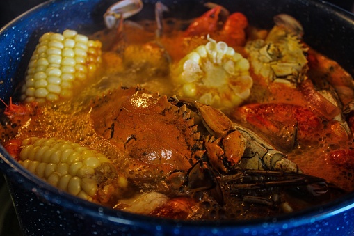 Large cobalt blue seafood pot cooking a traditional Cajun seafood boil including corn on the cob crabs crawfish potatoes lemon shrimp andouille sausage in a spicy broth