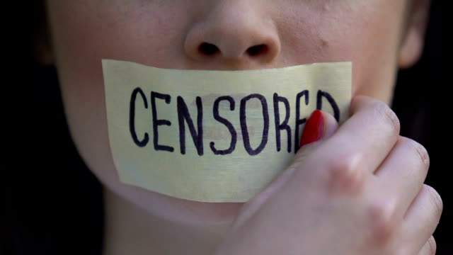 Censored written on tape, woman removing mouth sticker, speech freedom, pressure