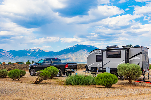 Taos, NM, USA-4 July 2018: A Ram pickup and a Camplite RV trailer parked in a desert campground, with a hazy mountain range behind.