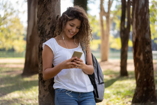 happy female student texting on her phone at the park - tree stream forest woods imagens e fotografias de stock