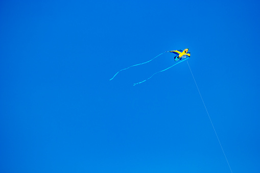 Yellow kite with long tails flying in the wind against a bright blue, unclouded sky
