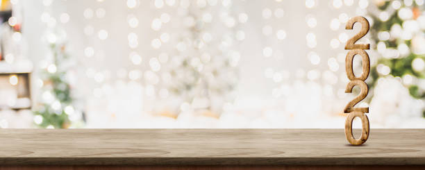 glückliches neues jahr 2020 bei woooden tischplatte mit abstrakten warmen wohnzimmer dekor mit weihnachtsbaum string licht unschärfe hintergrund mit schnee, urlaub hintergrund, mock up banner für die anzeige des produkts. - 2020 fotos stock-fotos und bilder