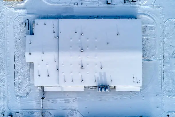 Large warehouse complex, the roof of the building is completely covered with snow. Aerial view.