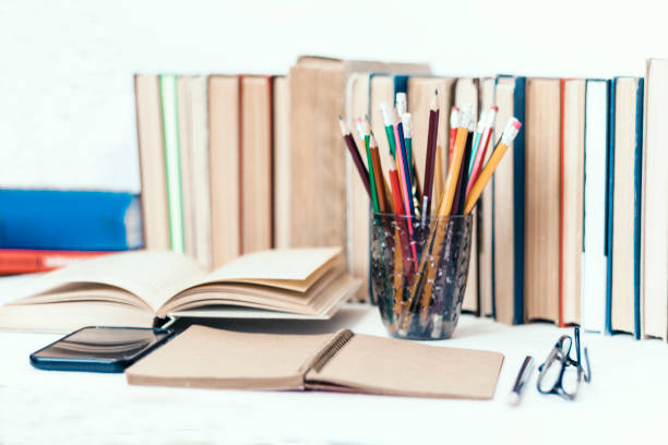 Books background, open book, smartphone, glasses and pencils holder on white wooden table in office for education learning concept