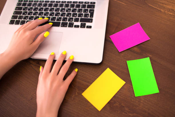 Woman typing text with hands and neon manicure on laptop keyboard.