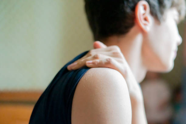 A close-up image of a woman’s hand massaging her bare shoulder and neck , set against a bright yellow background. The photo represents themes of self-care, relaxation, pain relief, and wellness, emphasizing a healthy and balanced lifestyle.