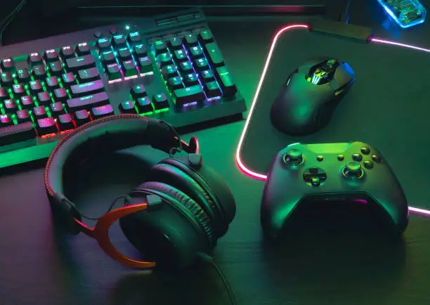 Photo of gamer work space concept, top view a gaming gear, mouse, keyboard, joystick, headset, mobile joystick, in ear headphone and mouse pad on black table background.