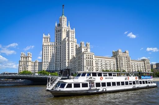 Moskow, Russia - may 20, 2019: Stalin's High-rise on Kotelnicheskaya embankment. Pleasure boat on Moscow river.