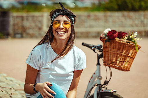 Happy smiling young woman is enjoying in a summer sunny day, beside the bike with flower basket.