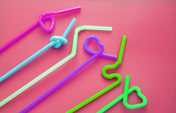 istock Colour plastic cocktail tubes with a flexible part, due to which they can be twisted into a knot or in a zigzag, or a heart shape, on a crimson background. Modern and trendy colors. Eco concept 1170089068