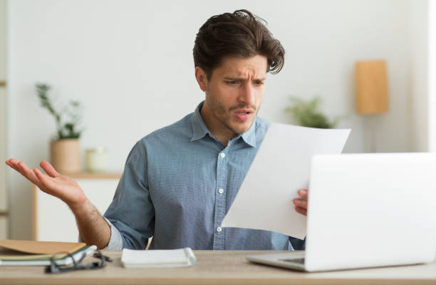 confused guy reading mail letter or debt notification indoors - frustration computer confusion businessman imagens e fotografias de stock