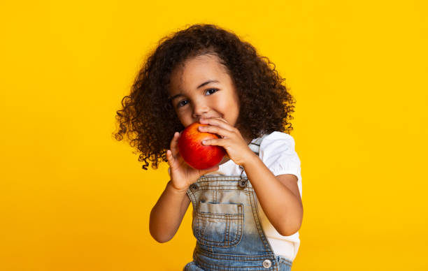 delicioso. pequeña niña afro comiendo manzana roja - apple healthy eating eating black fotografías e imágenes de stock