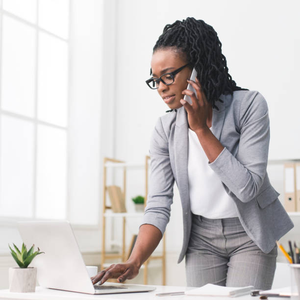 istock Afro Businesswoman Talking On Cellphone Typing On Laptop At Work 1170090123