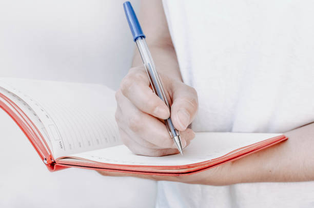 istock Woman's hands holding pen and red notepad on a white background. 1170098484