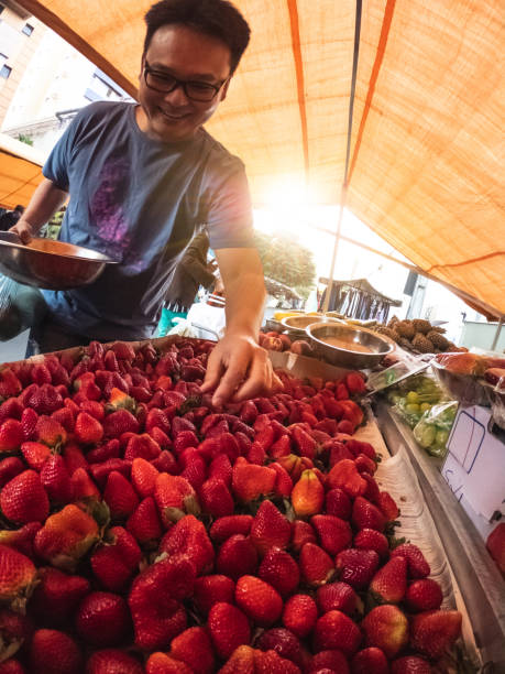 A close-up view of a large, vibrant pile of fresh strawberries, showcasing their bright red color and fresh green stems at a market