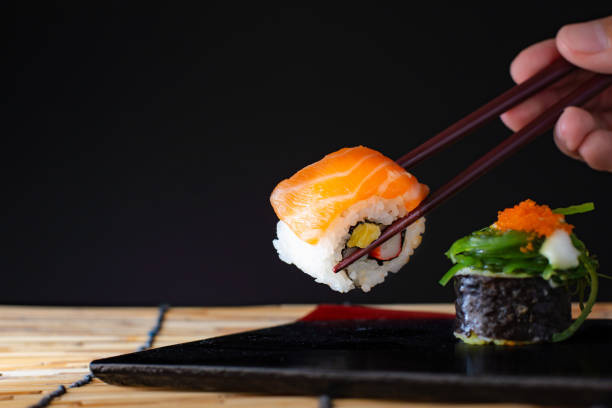 Sushi roll and salmon with chopsticks. Sushi roll japanese food in restaurant,Salmon sushi nigiri in chopsticks over black background. stock photo