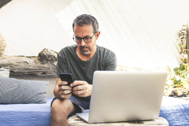 istock Business man working with laptop and smart phone during vacation. New technologies allow to communicate with remote friends everywhere. Male works busy sitting in the patio. New trends tech concept. 1170117541