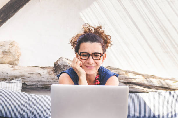 istock Smiling woman working with laptop during vacation. New technologies allow to communicate with remote connection. Female influencer writing travel blog sitting in patio. New trends tech concept. 1170117544