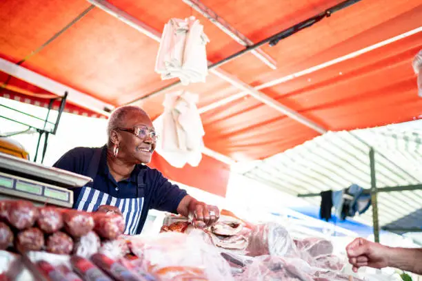 Photo of Senior woman offering product to a customer of her street market