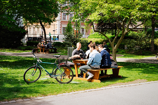 Vienna, Austria - May 8, 2019: People sitting on benches near table and bicycle in Park Resselpark at Handelsakademie, or HAK, or Vienna Business School on Karlsplatz in Old city center, Wien, Austria