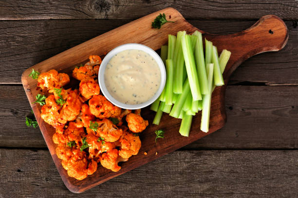 Healthy vegan cauliflower buffalo wings with celery and ranch dip, top view on a wood paddle board Cauliflower buffalo wings with celery and ranch dip. Top view on a wood paddle board. Healthy eating, plant based meat substitute concept. dipping stock pictures, royalty-free photos & images