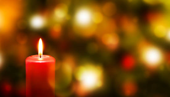 Red candle light Christmas candlelight on glowing flame sparkling green background blurred