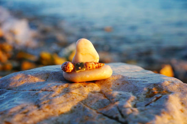 Sea background. Boat made from small stone on the big stone with blurred seacoast background and lit with sun rays at sunset