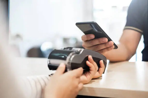 Customer using phone for payment to owner at cafe restaurant, cashless technology and credit card payment concept