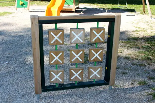 Photo of Retro vintage looking outdoor public playground equipment in shape of large wooden frame with x and 0 tiles used to play popular criss cross children game surrounded with playground sand