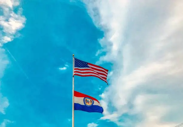 American and Missouri state flag against blue clouded sky