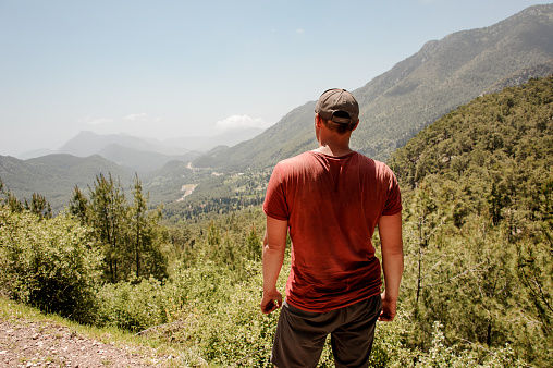 Broad-shouldered man in red t-shirt and cap posing in the turkish mountains