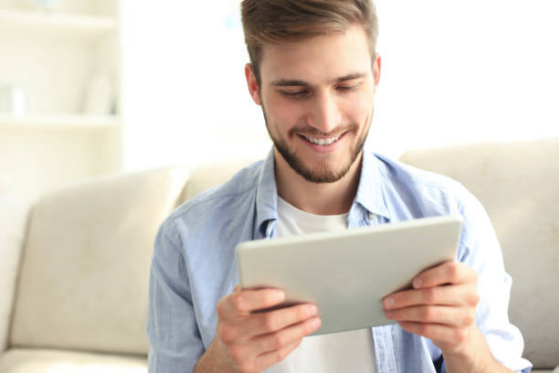 istock Handsome man is using a digital tablet and smiling while resting on couch at home. 1170149889