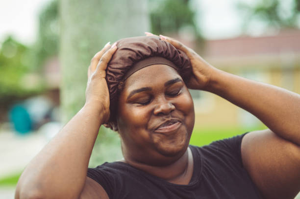African American woman in a hair cap Young confident African American woman wears a fabric hair cap for ethnic hair. She is happy and smiling candidly outdoors, casual and real person caught in a candid moment of real life do rag stock pictures, royalty-free photos & images