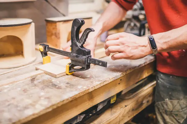 Carpentry workshop - a man fixes wooden parts with glued clamps